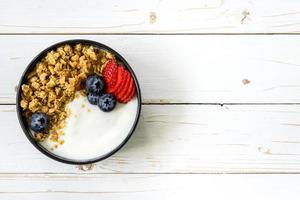 Schüssel von Granola mit Joghurt, frisch Beeren, Erdbeere auf Holz Tisch. foto