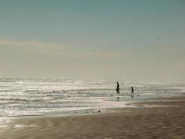 Silhouetten von Erwachsenen und zwei Kindern an einem Strand mit bewölktem blauem Himmel foto
