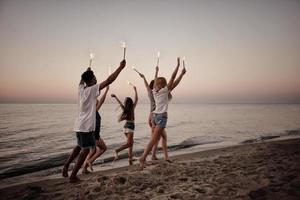 glücklich lächelnd freunde Laufen beim das Strand mit funkelnd Kerzen foto