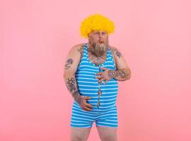 glücklich Mann mit Gelb Perücke und Badeanzug hat Magenschmerzen foto