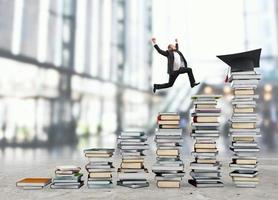 Geschäft Mann erreicht das Abschluss Hut Springen auf Haufen von Bücher. Konzept von Erfolg und Entschlossenheit auf Studie foto