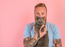Mann mit Bart und Tätowierungen streichelt ein grau Katze foto