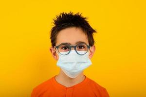 Porträt von ein Kind mit Gesicht Maske zum covid-19 Coronavirus. Gelb Hintergrund foto
