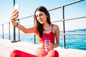 Frau Getränke Wasser und tut ein Selfie nach Fitness Übungen draussen foto