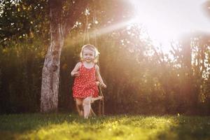 glücklich Baby lächelnd. wenig Mädchen Laufen im das Garten beim Sonnenuntergang draussen barfuß foto