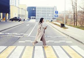 Frau halten Kaffee und Kreuzung das Straße beim Fußgänger Kreuzung gegen städtisch Stadt Hintergrund foto