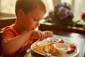 Junge Essen schnell Essen im ein Cafe. das Kind Essen Französisch Fritten mit Nuggets foto