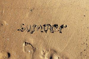 Wort Sommer- handgeschrieben auf das sandig Strand und Fußabdruck mit Kopieren Raum foto