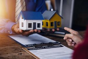 Immobilienmakler-Agent präsentiert und berät den Kunden bei der Entscheidungsfindung, unterzeichnet einen Versicherungsvertrag, kauft und verkauft ein Hausmodell, ein Hypothekendarlehensangebot für und eine Hausversicherung foto