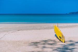 Surfbrett am Sommerstrand mit Sonnenlicht und blauem Himmel
