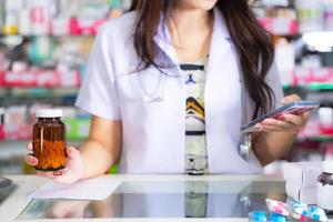 Der Apotheker hält eine Flasche Medizin in der Hand und benutzt Handys in der Apotheke foto