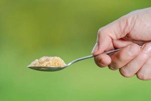 Hand hält einen Löffel mit Zucker auf einem natürlichen Hintergrund foto