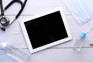Draufsicht des digitalen Tablets, des Händedesinfektionsmittels und des Stethoskops auf Tisch foto