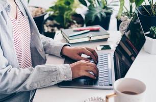 Frau, die an sauberem Naturarbeitsplatz zu Hause mit Laptop arbeitet foto