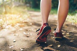 Frau, die Laufschuhe trägt und auf grünem Hintergrund der Natur läuft