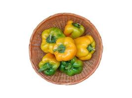 grüne und gelbe Paprika in einem Weidenkorb auf einem weißen Hintergrund