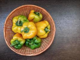 grüne und gelbe Paprika in einem Weidenkorb auf einem hölzernen Tischhintergrund foto