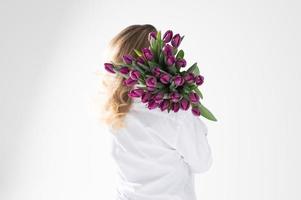 ein Mädchen im ein Hemd stellen ein Menge von Weiß und lila Tulpen von anders Sorten auf ihr Schulter foto