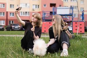 zwei komisch Mädchen sind Essen Eis Sahne und spielen mit ein pommerschen Hund. nehmen Selfies foto