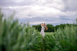 ein süß Mädchen mit lange Haar im ein Kleid läuft durch ein Weizen Feld foto