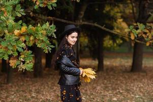 ein Mädchen im ein schwarz Hut hält Gelb Herbst Blätter im ihr Hände foto