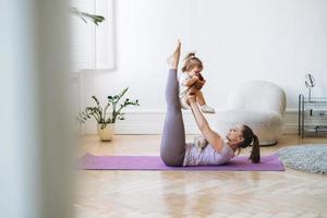 junge frau passte mutter mit babymädchen, das zu hause fitness auf der matte macht foto