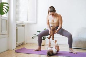 junge frau passte mutter mit babymädchen, das zu hause fitness auf der matte macht foto