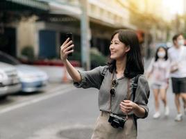 jung asiatisch Frau Rucksack Reisender mit Handy, Mobiltelefon Telefon, genießen Straße kulturell lokal Ort. Reisender Überprüfung aus Seite Straßen. foto