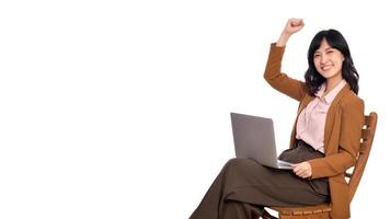 glücklich jung Geschäft asiatisch Frau feiern auf ihr Erfolg. während ihr mit Laptop Sitzung auf hölzern Stuhl isolieren auf Weiß Hintergrund foto