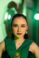 ein schön asiatisch Frau im ein Grün Kleid hat ein sehr exotisch Gesicht mit Ohr und Körper Schmuck während foto