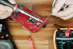 Techniker Mann halten Eisen löten und reparieren das Schaltkreis Tafel durch Löten. elektrisch Arbeit Konzept foto