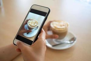 Hand halten Handy, Mobiltelefon Telefon oder Zelle Telefon Digital Kamera nehmen Foto zu Tasse von heiß Kaffee. zu aktualisieren zu Sozial