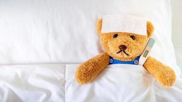 der teddybär schlief mit hohem fieber im bett. zusammen mit einem Thermometer. foto