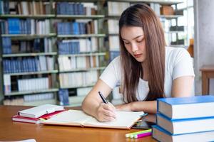 schön asiatisch weiblich Studenten tun ihr Hausaufgaben und Bericht im das Bibliothek. foto