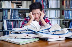 asiatisch männlich Studenten sind müde und betont mit lesen ein Menge zu bereiten zum das Prüfung. foto