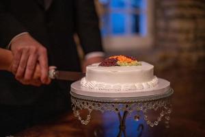 Braut und Bräutigam schneiden eine kleine moderne Hochzeitstorte an der Rezeption