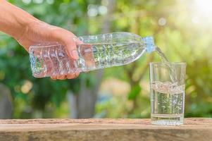 Flasche Trinkwasser und Glas mit natürlichem Hintergrund foto