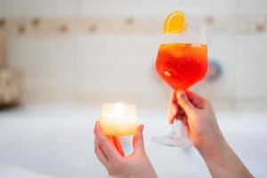 Frau halten Glas von Aperol Spritz oder coctail im Bad mit Aroma Kerze. foto