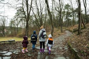 zurück von Mama und Kinder mit Rucksäcke Gehen entlang das Wald Stein Straße nach Regen zusammen. foto