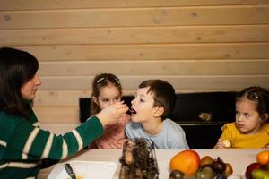 Mutter mit drei Kinder Essen Früchte im hölzern Land Haus auf Wochenende. foto