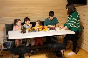 Mutter mit vier Kinder Essen Früchte im hölzern Land Haus auf Wochenende. Mama schneidet das Gelb Drachen Frucht. foto