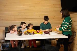 Mutter mit vier Kinder Essen Früchte im hölzern Land Haus auf Wochenende. Mama schneidet das Gelb Drachen Frucht. foto