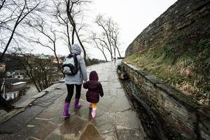 Mutter und Mädchen gehen oben das nass Pfad zu ein uralt mittelalterlich Schloss Festung im Regen. foto