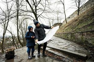 Vater und Sohn Tourist aussehen beim Karte, Stand auf nass Pfad zu ein uralt mittelalterlich Schloss Festung im Regen. foto