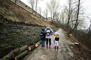 Mutter und Kinder gehen oben das nass Pfad zu ein uralt mittelalterlich Schloss Festung im Regen. foto