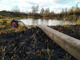 elektrisch Wasser Pumpe platziert auf das Teich Küste. tragbar Wasser Pumpe auf Land Teich Küste. Löschen ein natürlich Feuer. Verbrennung Boden und Vegetation. Torf Feuer. foto