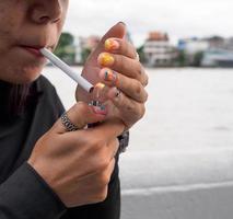 Porträt Frau Mädchen Teen jung Asien einer Person tragen ein Hut und lange schwarz Haar tragen ein schwarz Hemd Hand halt Rauchen Zigarette Weiß Farbe Stehen draussen durch das Mauer draussen foto