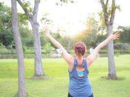 Porträt von ein schön asiatisch Frau im Sportbekleidung, Stehen mit ihr zurück, Dehnen Vor ausüben draussen im das Park im das Morgen zu leisten ein gesund Lebensstil. gesund Erwärmen oben foto