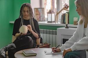 ein weiblich Psychologe funktioniert im ihr Büro mit ein jung Klient mit Dreadlocks auf ihr Kopf, Wer ist halten ein Attrappe, Lehrmodell, Simulation von ein Schädel. Probleme von Generation z im Leben, im Kommunikation. foto