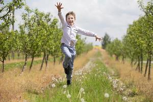 ein glücklich Junge läuft durch das Frühling Garten und springt hoch. Ferien haben begonnen. foto